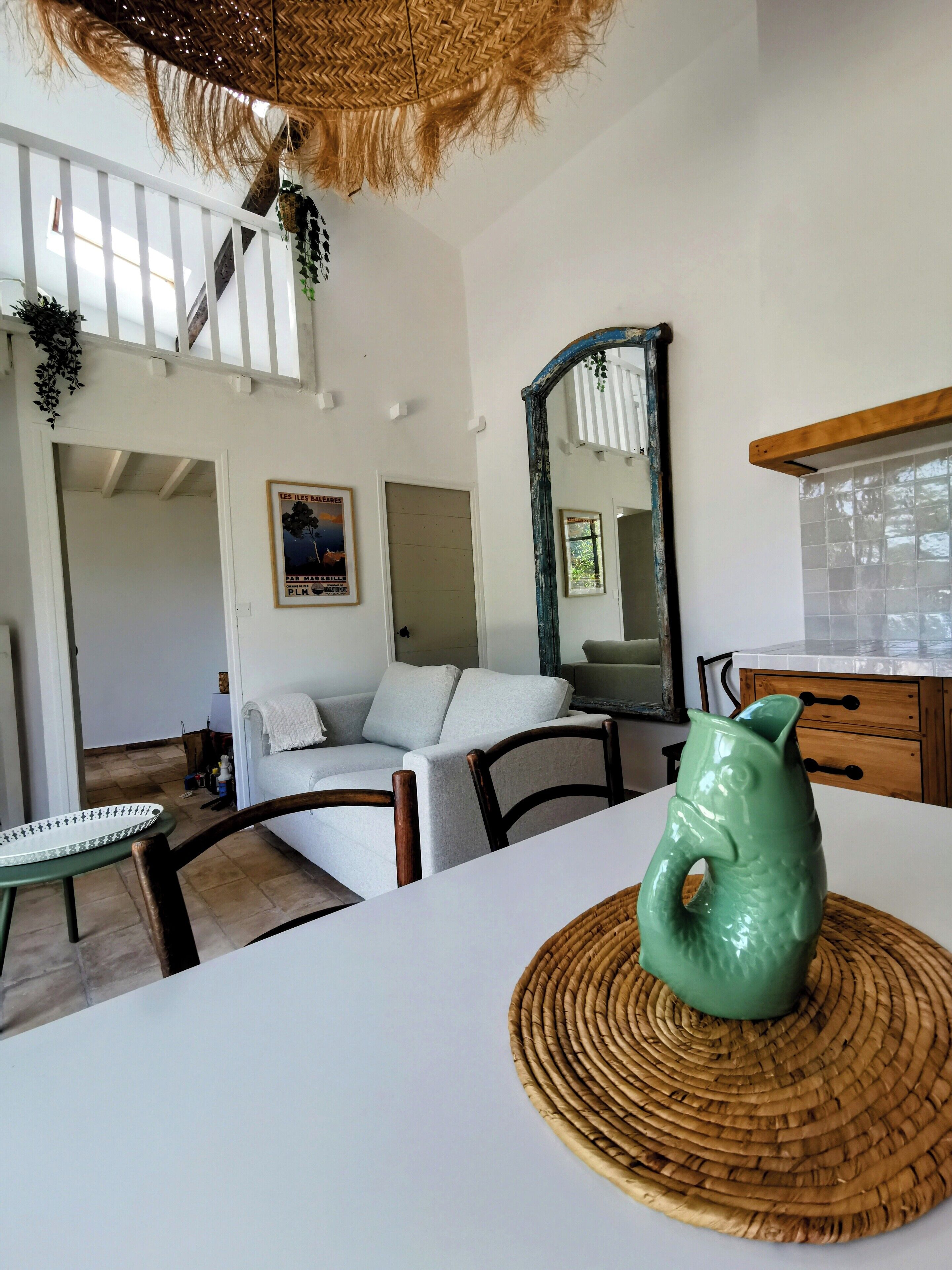 A modern living room with a white sofa, a green ceramic pig, and a woven placemat on a dining table.