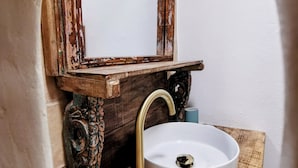 A rustic bathroom with a white sink, a brass faucet, and a wooden shelf. - Mas en pierre, piscine et jardin privés, 2ch, 5 pers, 10min du Pont du Gard (Meynes)