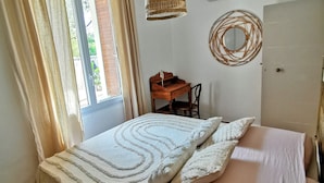 A bedroom with a bed, a hanging light fixture, a wooden desk, and a wall-mounted mirror. - Mas en pierre, piscine et jardin privés, 2ch, 5 pers, 10min du Pont du Gard (Meynes)