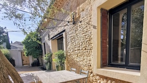 An outdoor dining area with a table and chairs, a stone wall, and a window. - Mas en pierre, piscine et jardin privés, 2ch, 5 pers, 10min du Pont du Gard (Meynes)