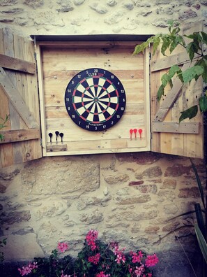 Een dartbord bevestigd aan een houten wand met een stenen voetstuk, omringd door planten en bloemen.