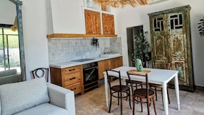 A modern kitchen with wooden cabinets, a dining table, and a hanging light fixture. - Mas en pierre, piscine et jardin privés, 2ch, 5 pers, 10min du Pont du Gard (Meynes)