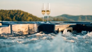 Two glasses of white wine on a hot tub with a mountainous landscape in the background.