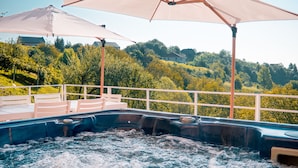 A hot tub area with two umbrellas, surrounded by a railing, overlooking a lush green landscape.