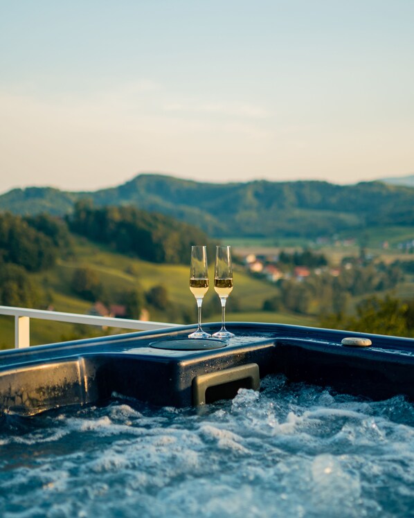 Dos copas de vino blanco en un jacuzzi con una vista panorámica de colinas ondulantes y un pueblo lejano.
