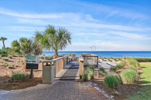 A paved pathway leading to a beach with palm trees and a wooden boardwalk. - Adagio B103 | Beach Front |Bunk room | Private Beach |Resort Style Pool YFAB (Santa Rosa Beach)