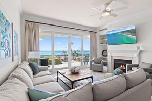 A living room with a sofa, coffee table, TV, fireplace, and a balcony with a view of the ocean. - Adagio B103 | Beach Front |Bunk room | Private Beach |Resort Style Pool YFAB (Santa Rosa Beach)