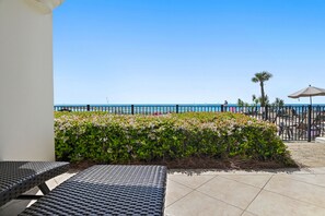 A patio area with outdoor seating, a view of the sea, and a palm tree. - Adagio B103 | Beach Front |Bunk room | Private Beach |Resort Style Pool YFAB (Santa Rosa Beach)