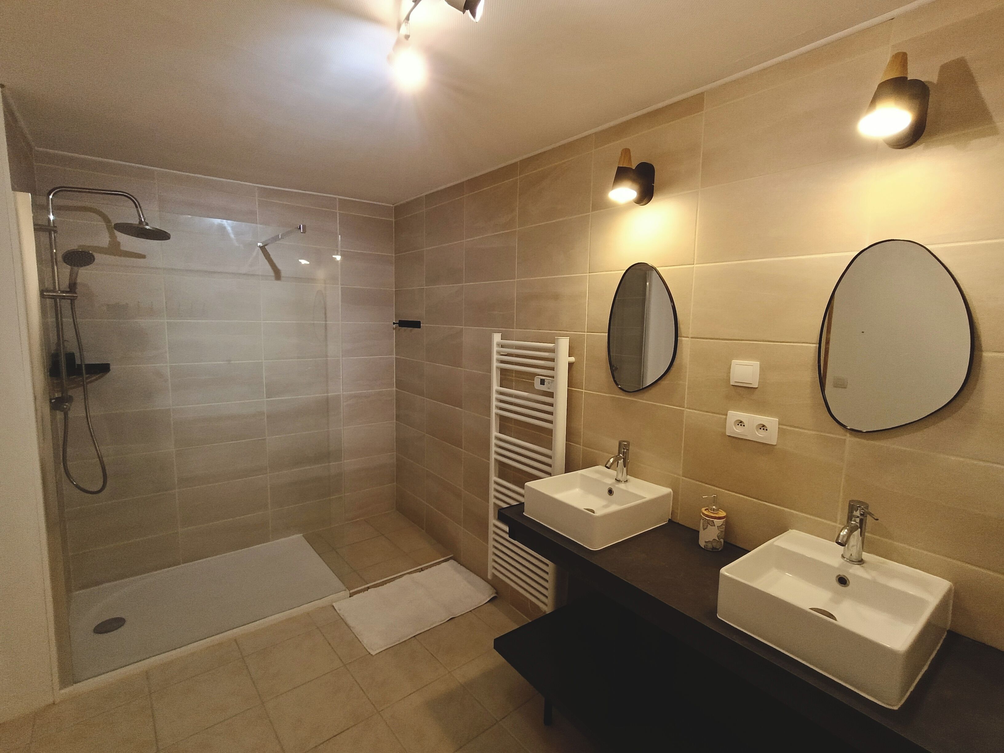 Une salle de bain moderne avec une douche à parois de verre, deux lavabos, un miroir et un porte-serviettes.