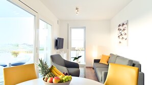 A modern living room with a dining table, a sofa, and a TV mounted on the wall. - Holiday Apartment 'Dinkelbach Traumblick 3C' with Lake & Mountain View, Balcony, Wi-Fi (Wasserburg (Bodensee))