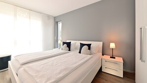 A modern bedroom with a large bed, bedside tables, and a window. - Holiday Apartment 'Dinkelbach Traumblick 3C' with Lake & Mountain View, Balcony, Wi-Fi (Wasserburg (Bodensee))