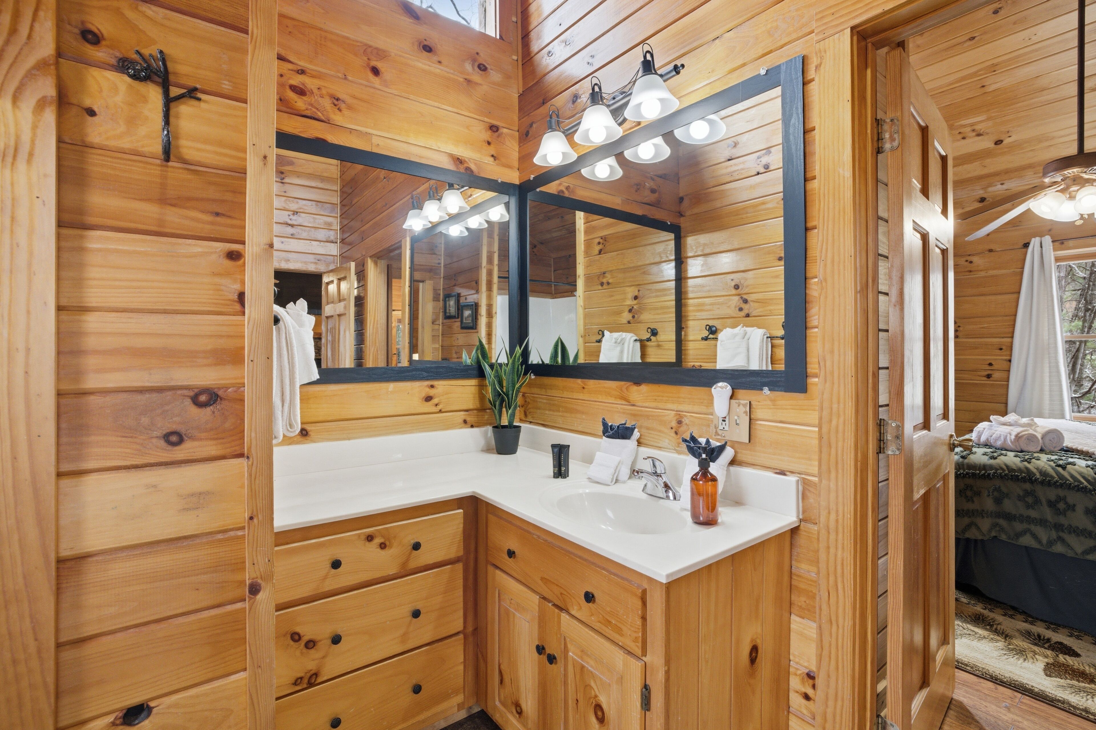 Baño de cabaña de madera con un espejo grande, lavabo blanco, armarios de madera y zona de ducha.