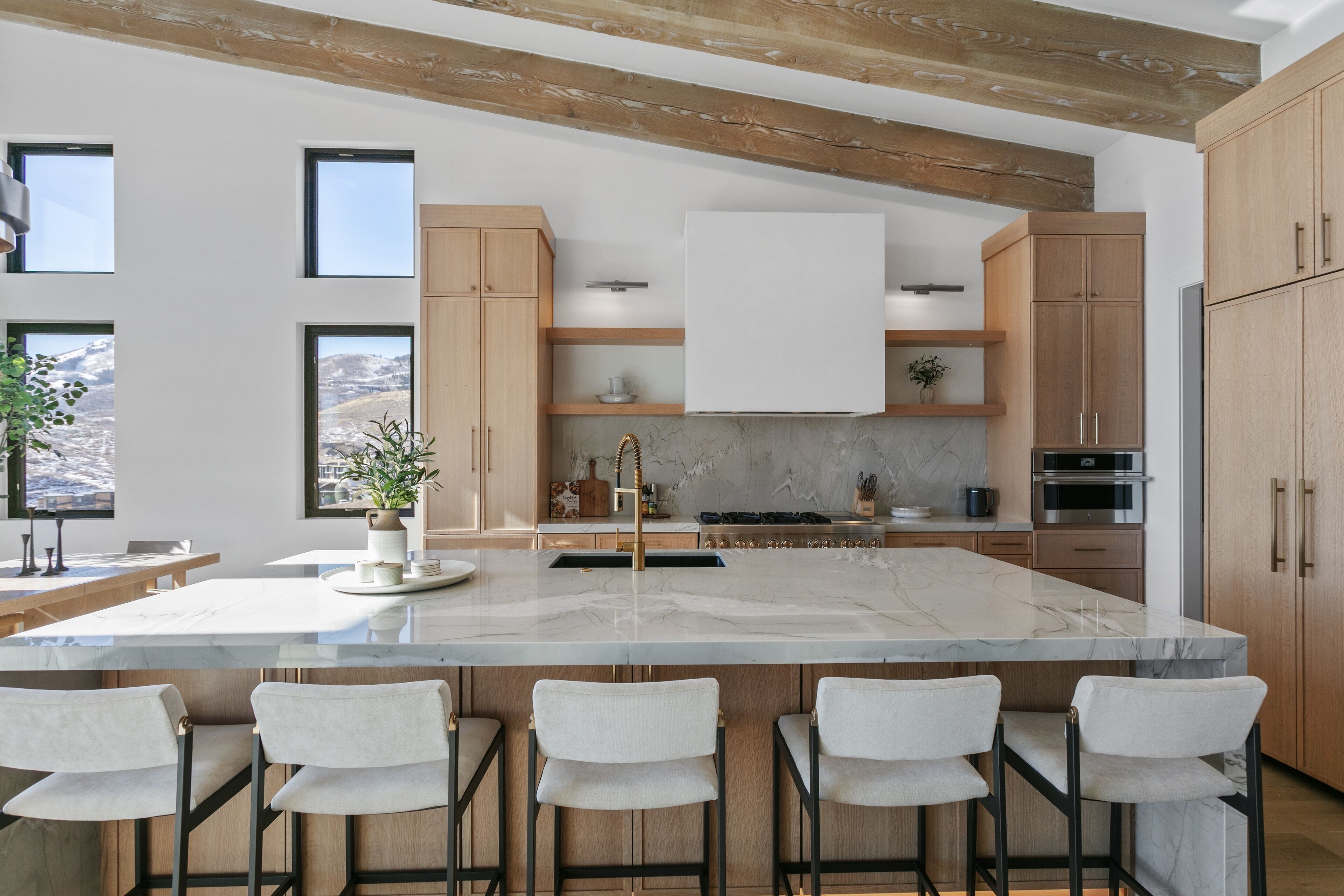 A modern kitchen with a large island, wooden cabinets, and a marble countertop.