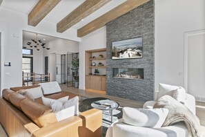 A modern living room with a stone accent wall, a fireplace, and a large window. - Luxury Deer Valley East Village Retreat Hot Tub 4 Bedroom Home (Heber City)