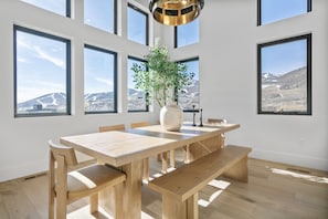 A spacious dining area with a wooden table and benches, large windows offering mountain views, and a modern pendant light. - Luxury Deer Valley East Village Retreat Hot Tub 4 Bedroom Home (Heber City)