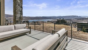A terrace with a stone column, a white sofa, and a view of a lake and distant mountains. - Luxury Deer Valley East Village Retreat Hot Tub 4 Bedroom Home (Heber City)