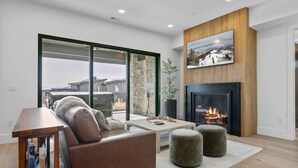 A modern living room with a fireplace, a sofa, a coffee table, and a view of a snowy landscape through large windows. - Luxury Deer Valley East Village Retreat Hot Tub 4 Bedroom Home (Heber City)