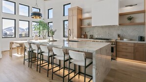 A modern kitchen with a large island, bar stools, and a view of the mountains. - Luxury Deer Valley East Village Retreat Hot Tub 4 Bedroom Home (Heber City)