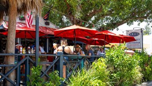 An outdoor dining area with red umbrellas, a wooden fence, and greenery. - PRIVATE BEACH ACCESS, SPRING-FED LAKE, WALK TO SIESTA KEY VILLAGE! (Siesta Key)
