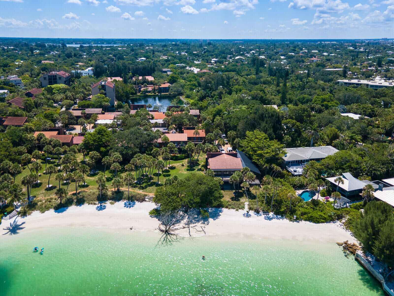 An aerial view of a coastal resort with multiple buildings, a sandy beach, and clear turquoise waters.