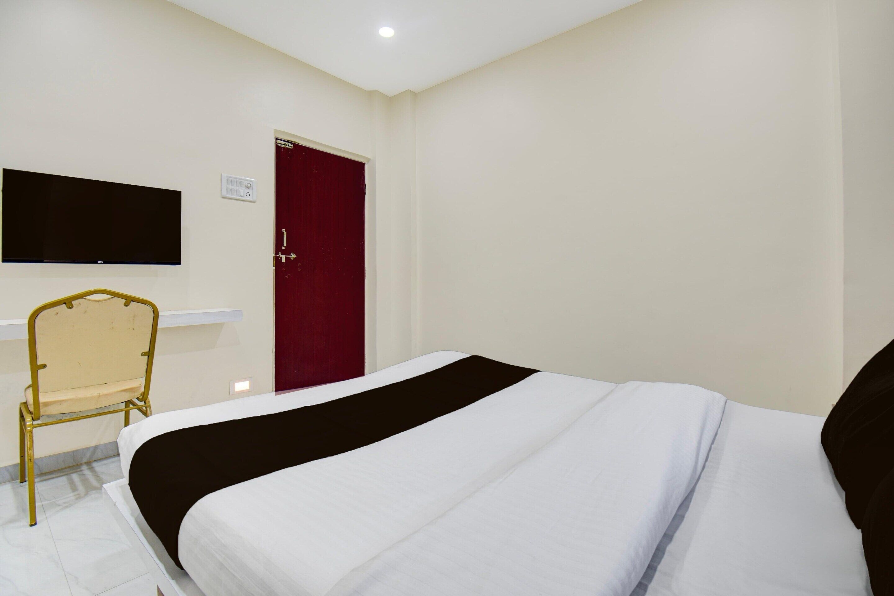 A hotel room with a bed, a chair, a television mounted on the wall, and a red door.