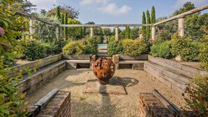 A garden with a central decorative metal sculpture, surrounded by neatly arranged flower beds and a pergola structure. - Stunning English country house in rural Kent (Eastry)
