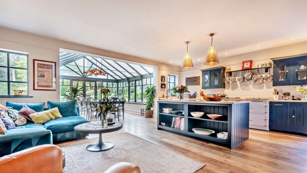 A spacious living room with a blue sofa, a coffee table, and a leather chair. A large window offers a view of the outdoors. - Stunning English country house in rural Kent (Eastry)