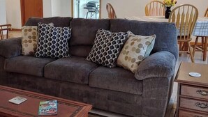Ein Wohnzimmer mit Sofa, gemusterten Kissen, einem Couchtisch, einem Esstisch mit Stühlen und einem Bild an der Wand.