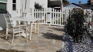 Eine Terrasse mit Tisch und Stühlen, ein weißer Zierzaun und eine kleine Gartenanlage.