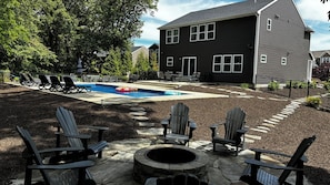 En have med swimmingpool, Adirondack-stole, bålsted og et hus med mørk facade.