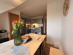 Eine moderne Küche mit grauen Schränken, einer Mikrowelle und einer Kaffeemaschine. Ein Esstisch mit einer Tulpenvase und einem Brotkorb.