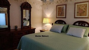 Une chambre à coucher comprenant un lit, une commode, un miroir, une lampe et deux tableaux encadrés accrochés au mur.