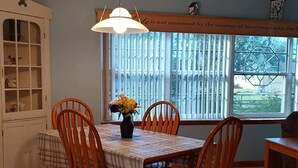 Un coin repas avec une table dressée pour quatre personnes, entourée de chaises en bois, d’un vase rempli de fleurs et d’un luminaire suspendu.