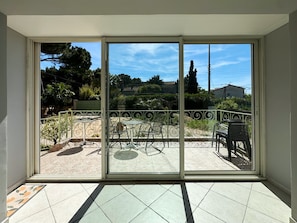 A room with a sliding glass door leading to an outdoor patio with a tiled floor, metal railing, and outdoor furniture.
