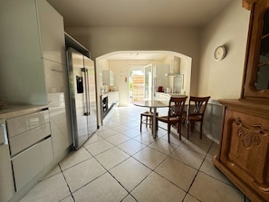 A kitchen with white cabinets, a stainless steel refrigerator, a dining table with chairs, and a wooden cabinet with carved details.