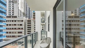 A balcony with a chair, a small table, and a view of surrounding high-rise buildings. - 2BR Suite | Rooftop Pool | Walk to Bayside (Miami)