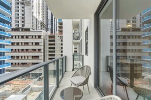 A balcony with a chair, a small table, and a view of surrounding high-rise buildings. - 2BR Suite | Rooftop Pool | Walk to Bayside (Miami)