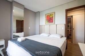 A hotel room with a large bed, a bedside table, a mirror, and a painting on the wall. - Building w/ Pool in Front of the Beaches of Bacutia and Peracanga - Emqs (Guarapari)