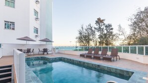 A rooftop pool area with a clear view of the sea, surrounded by lounge chairs and umbrellas. - Building w/ Pool in Front of the Beaches of Bacutia and Peracanga - Emqs (Guarapari)