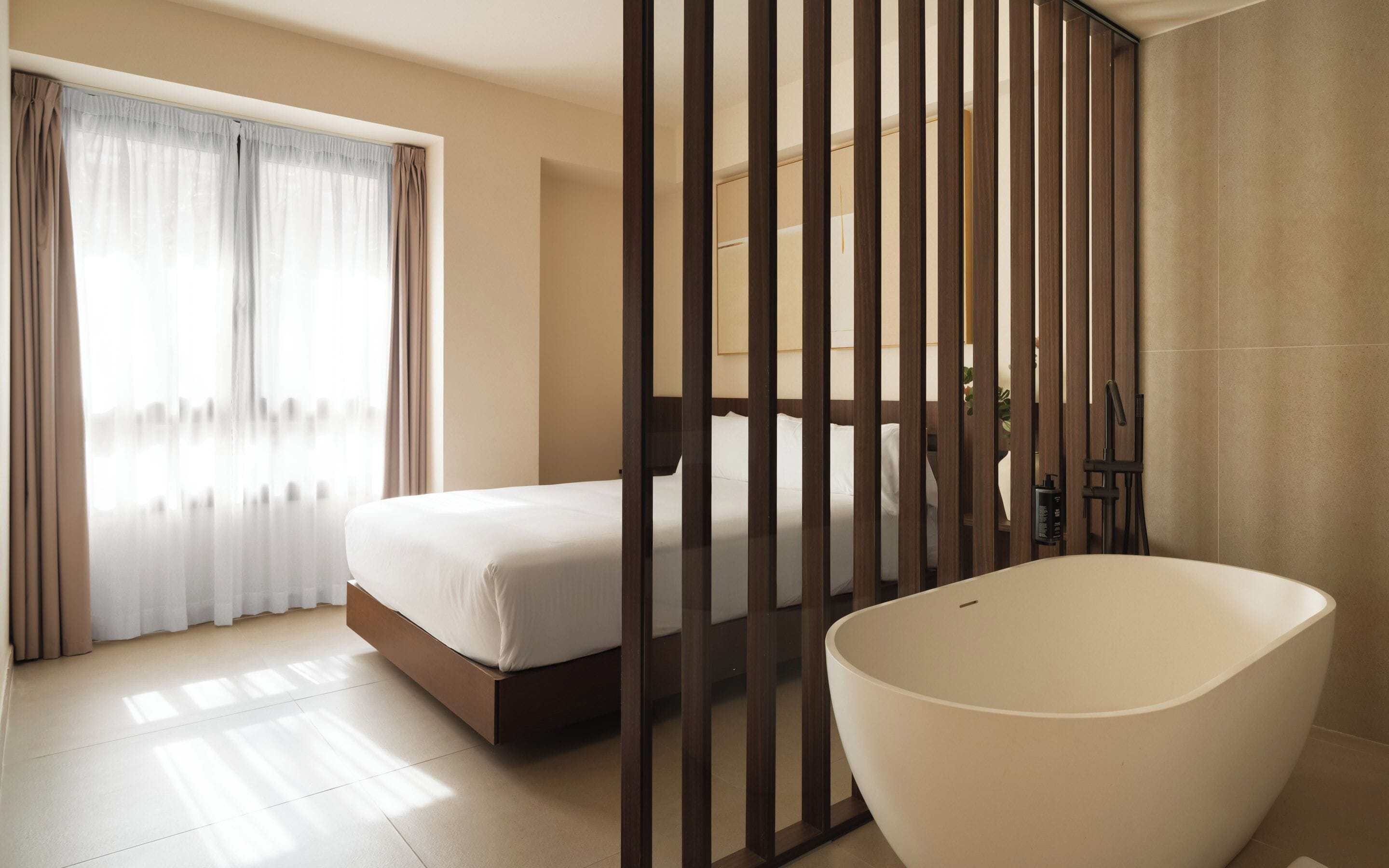 Habitación de hotel moderna con una cama grande, una bañera y vistas a través de un panel de madera.