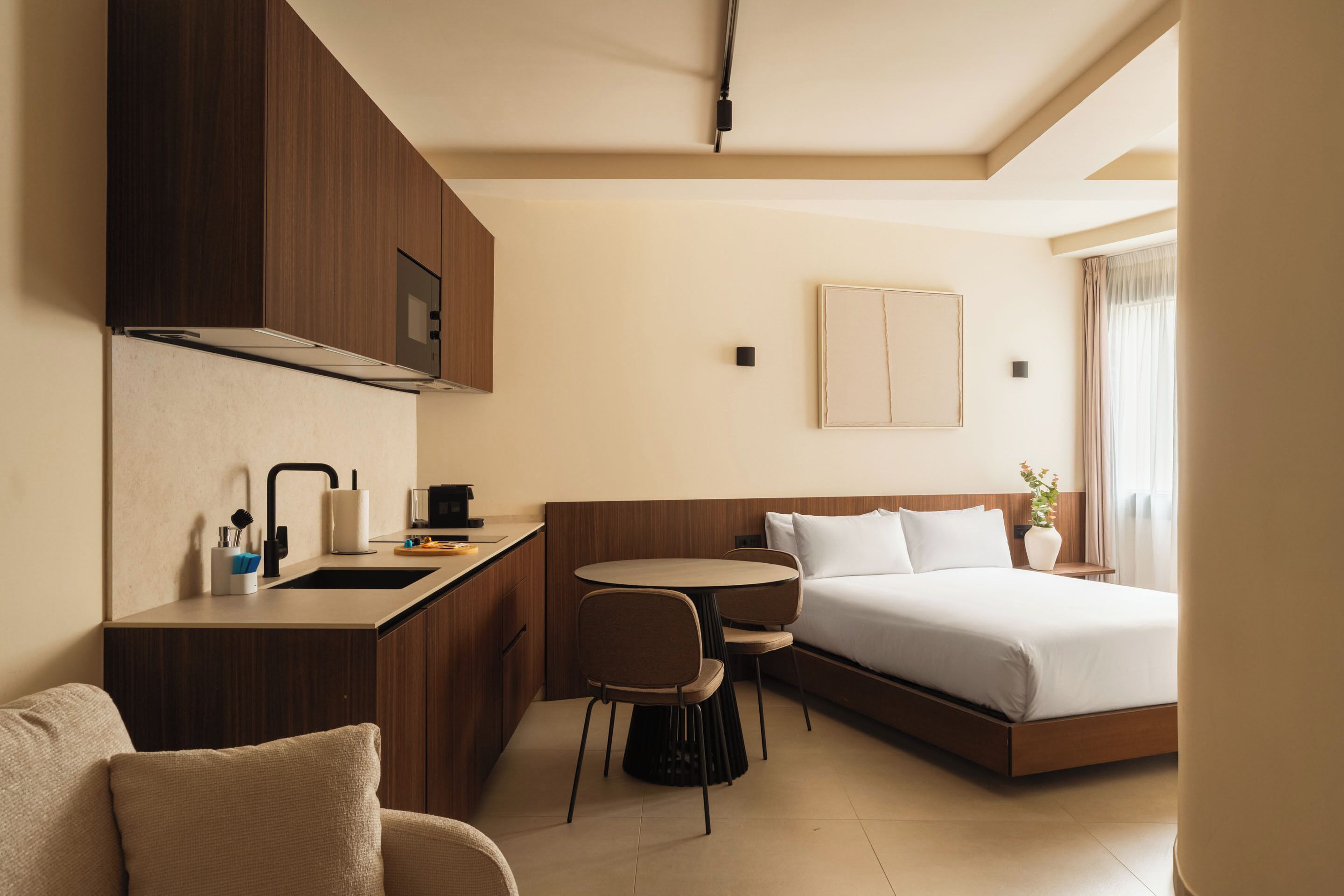 A hotel room with a kitchenette, a bed, a sofa, and a dining area.