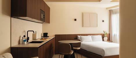 A hotel room with a kitchenette, a bed, a sofa, and a dining area.
