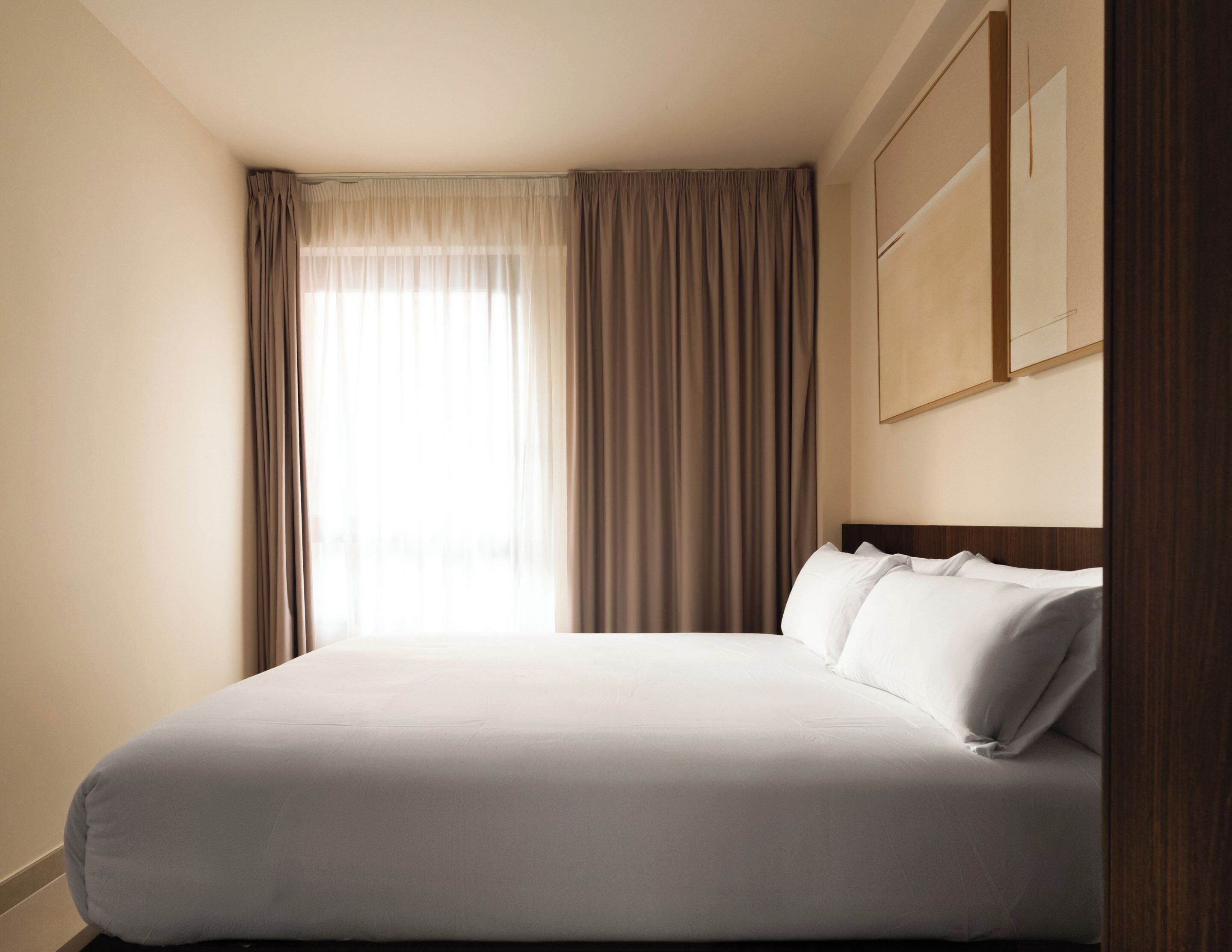 A hotel room with a bed, curtains, and a painting on the wall.