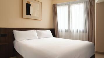 Una cama bien hecha en una habitación de hotel, con una obra enmarcada encima y cortinas translúcidas en la ventana.