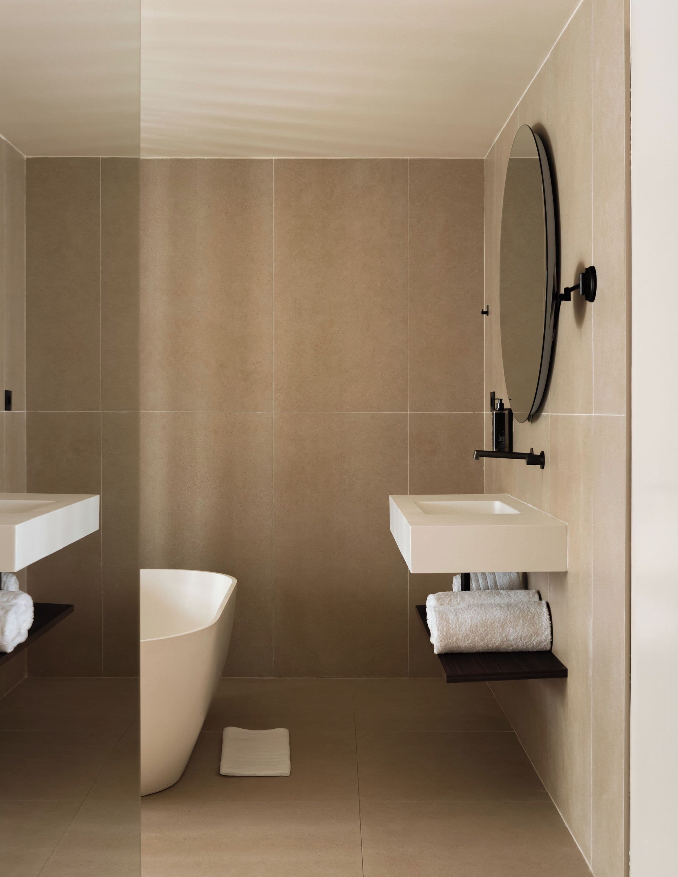 A modern bathroom with a freestanding bathtub, two sinks, a mirror, and a towel rack.