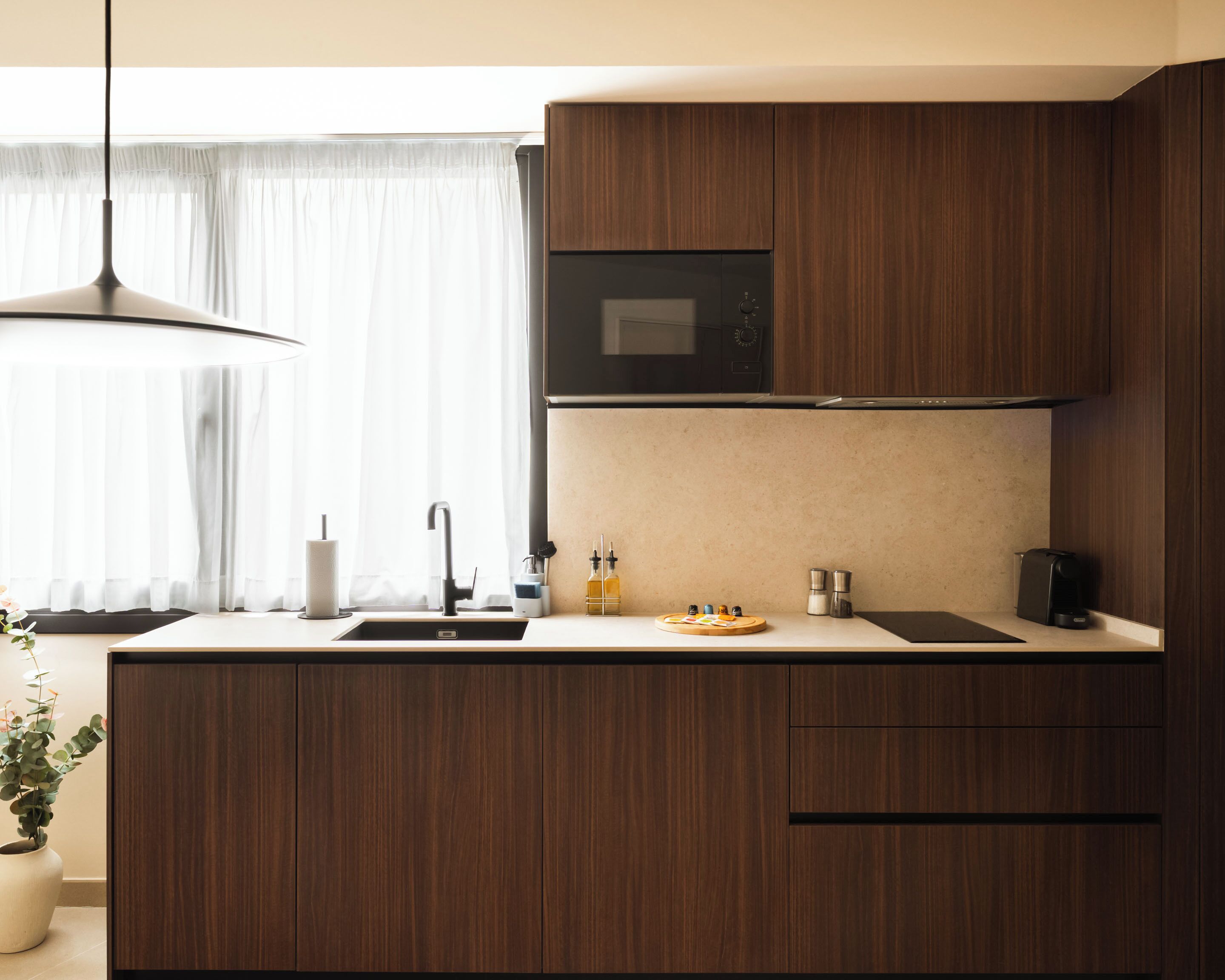 Una cocina moderna con armarios de madera, microondas integrado, un lavamanos y una cafetera.