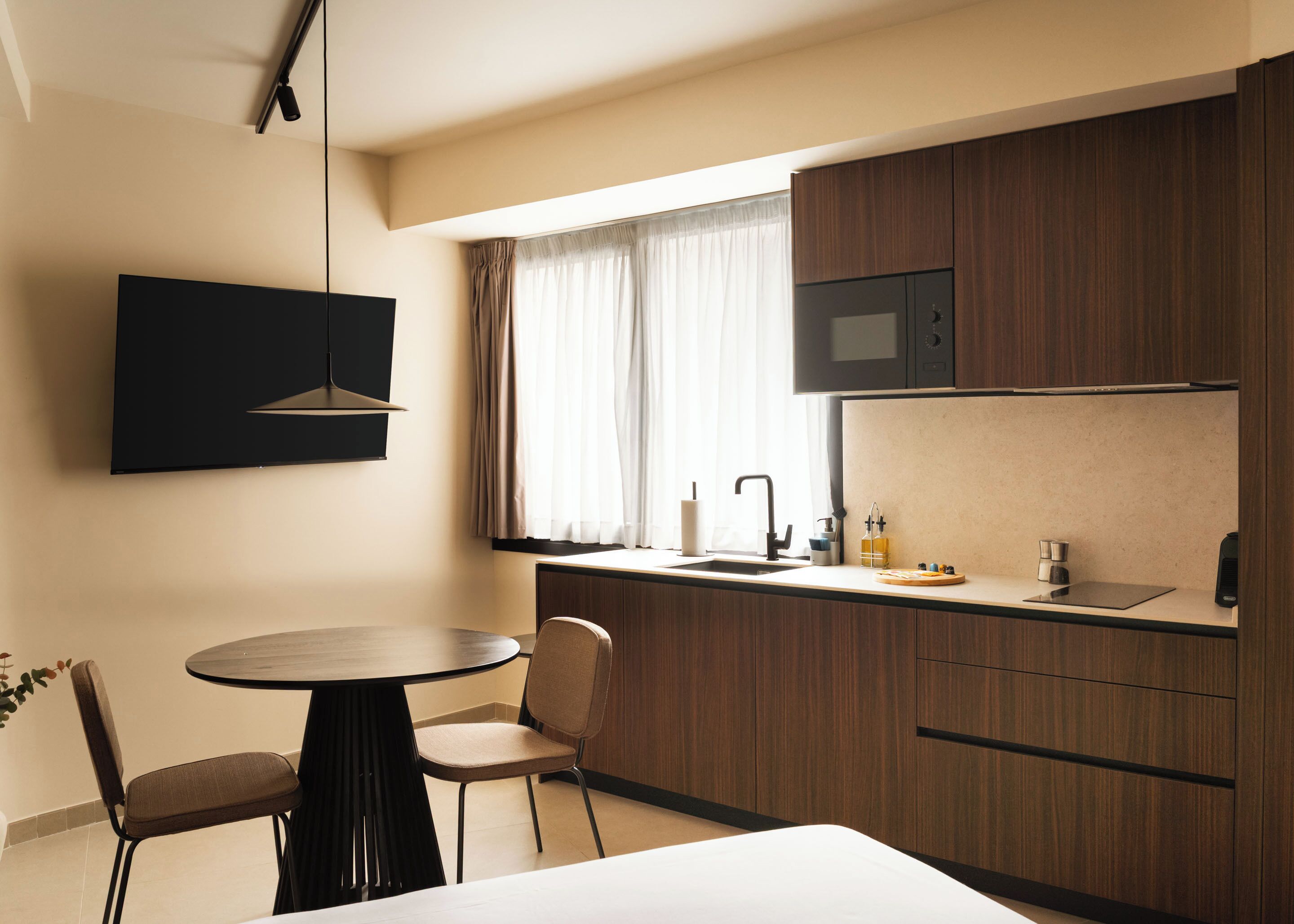 A modern kitchen with a dining area, including a round table, two chairs, a built-in microwave, and a window with curtains.