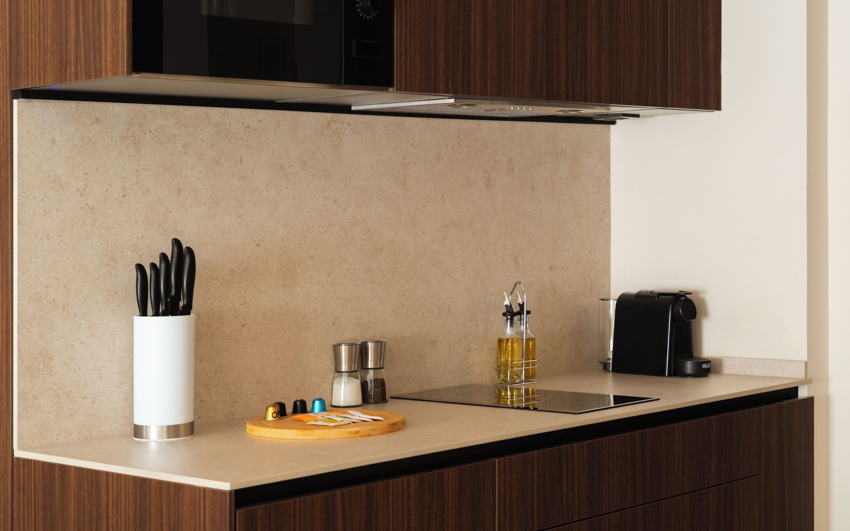 A kitchen with a countertop, a coffee machine, a bottle of oil, a cutting board, and a knife holder.