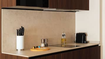 A kitchen with a countertop, a coffee machine, a bottle of oil, a cutting board, and a knife holder.