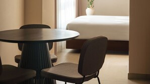 Ein modernes Hotelzimmer mit einem runden Esstisch, Stühlen, einer Hängelampe, einem Bett und einer Topfpflanze.